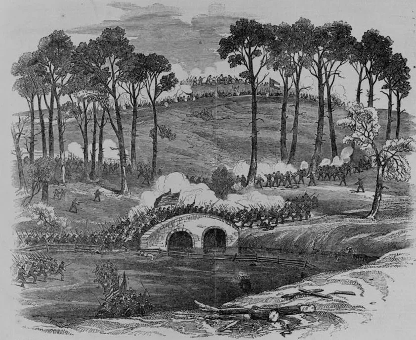 Black-and-white Civil War engraving showing Burnside’s troops charging across a stone bridge over Antietam Creek, with smoke rising around the span and soldiers advancing over the wooded hills beyond. Tall trees frame the rolling battlefield, giving the scene a dramatic, crowded sense of movement.