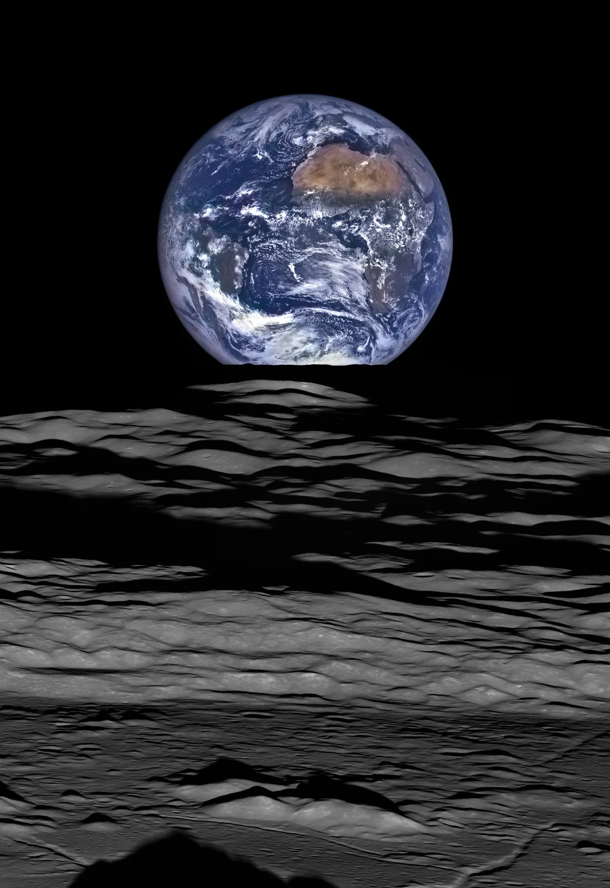 Earth hangs low over Compton Crater’s gray, rippled lunar surface, with Africa and swirling cloud bands visible against a black sky. The foreground is a rugged expanse of shadowed basalt-like terrain, lit with stark, silvery highlights.