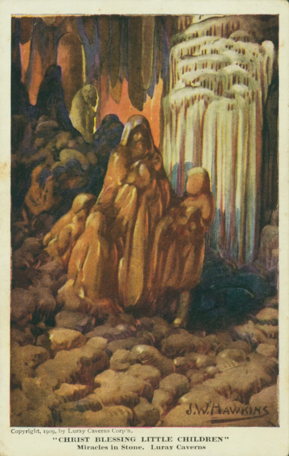 A warm, sepia-toned cave chamber shows a rock formation shaped like Christ blessing little children, surrounded by hanging stalactites and a massive white flowstone curtain on the right. The uneven stone floor fills the foreground, giving the scene a cathedral-like, underground feel.