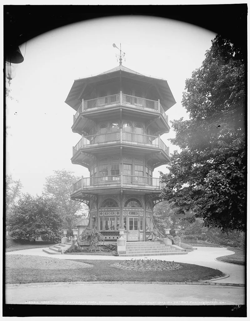 The Victorian wooden pagoda rises in stacked octagonal tiers, with wraparound balconies, arched windows, and a weather vane on top, framed by trees and curving park paths. Soft light and the black-and-white image give it a quiet, historic feel.