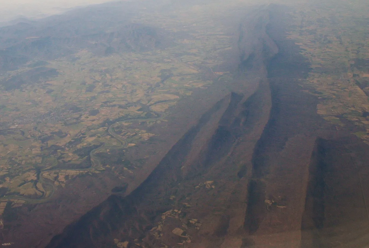 Sweeping aerial view of the Shenandoah Valley, with the river winding through a series of deep oxbow bends beside Massanutten Mountain. Soft golden light and haze flatten the distant ridges while patchwork fields fill the valley below.