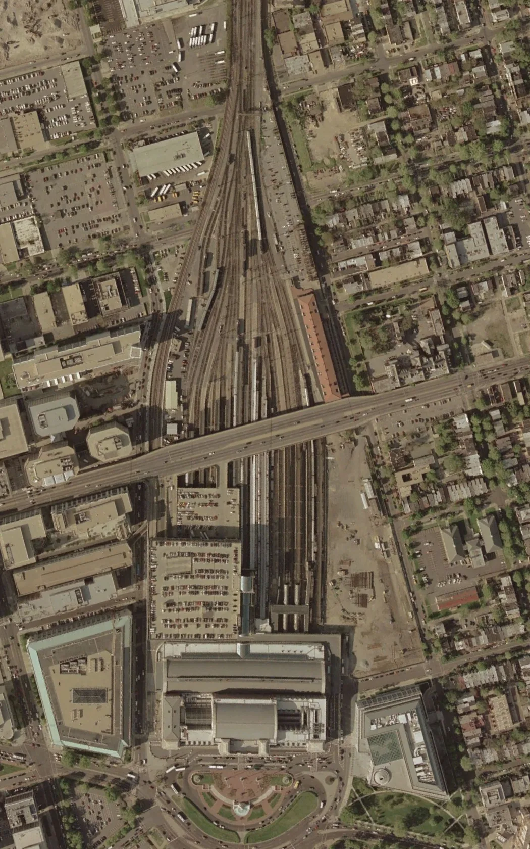 A straight-down aerial view shows Union Station’s long rail yard and platform tracks fanning north from the station roof, with the grand building at the bottom of the frame. Surrounding blocks of parked cars, low-rise buildings, and a busy road crossing the tracks reveal the dense city grid around it.